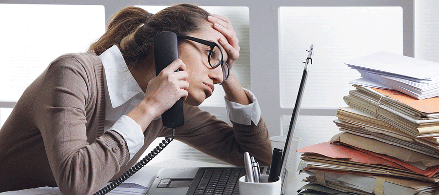 Woman sitting at a desk on the phone staring at computer and looking stressed out