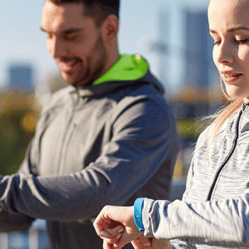 Man and woman walking outside looking at their smart watch